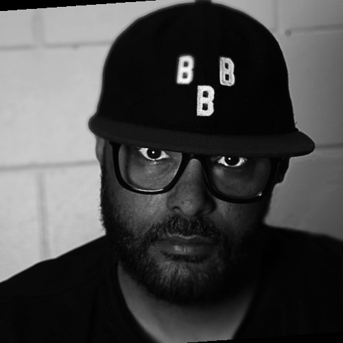 A black and white headshot of DA Bullock, who is looking at the camera. He wears a black cap with the letters "B B B" in white.